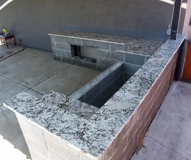Outdoor kitchen block base topped with white and gray granite countertops on a concrete patio